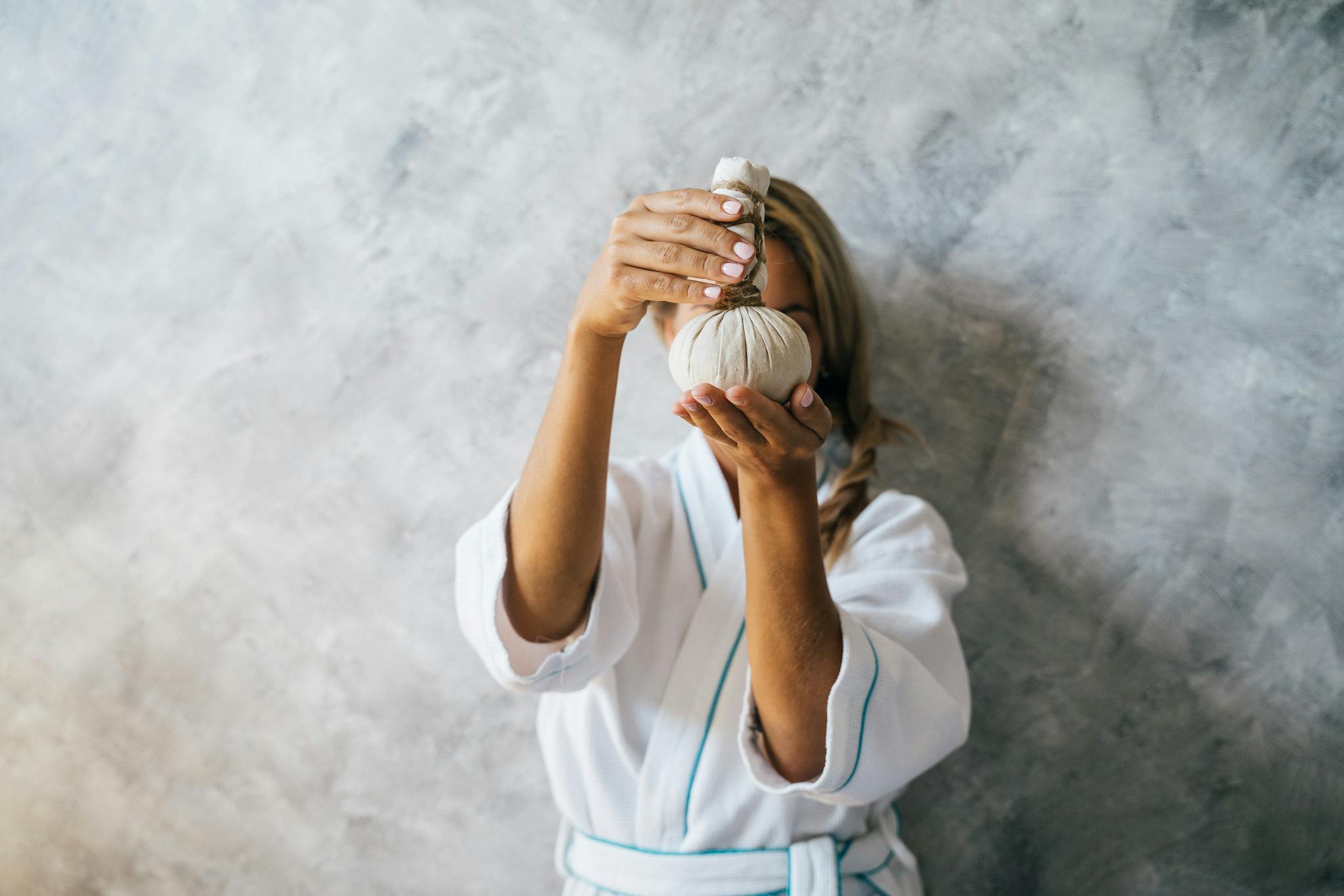 Woman in spa robe holding herbal compress for a rejuvenating spa treatment.